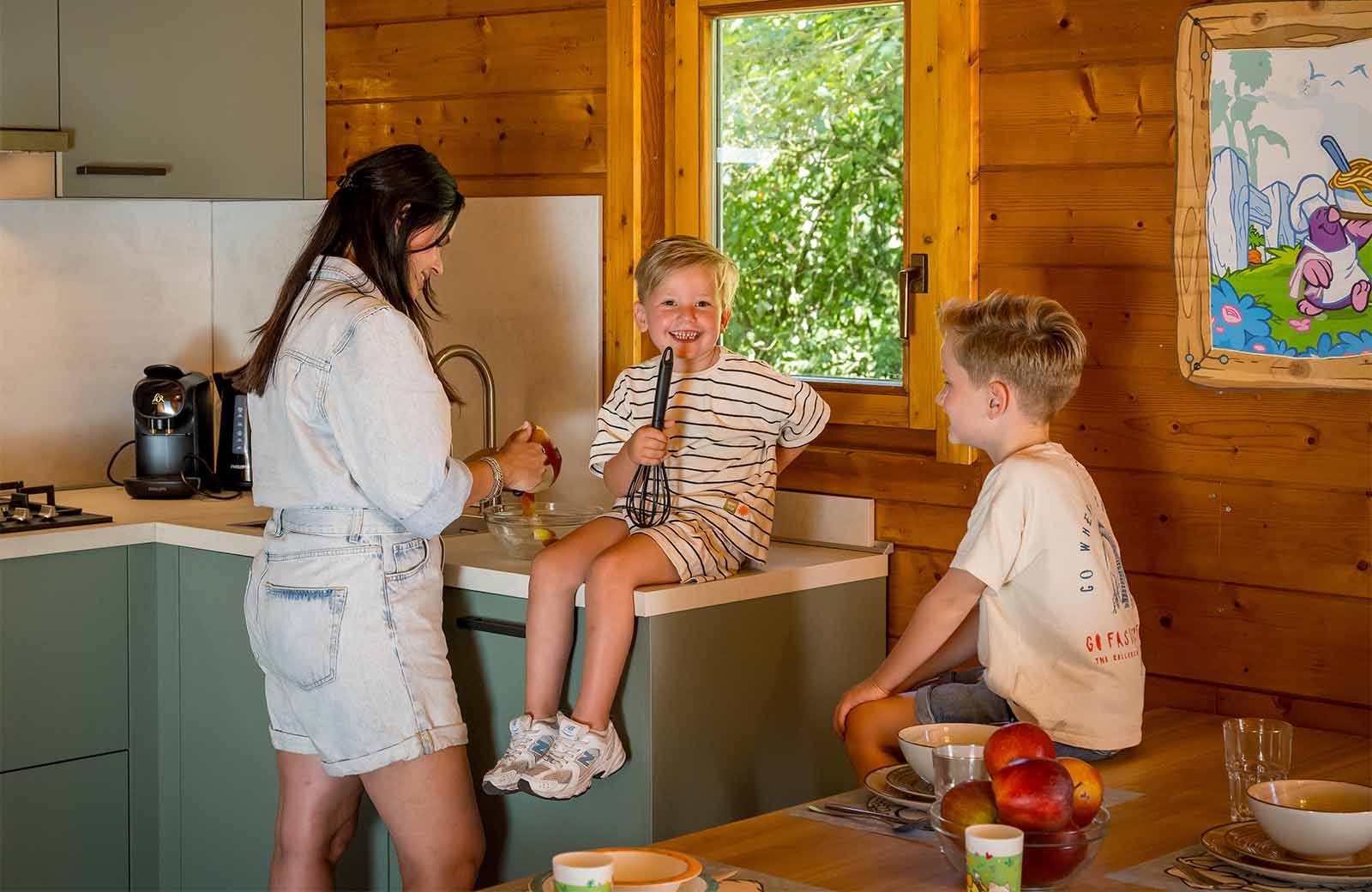 Molletjes Boshut keuken in de Tovertuin, kind zit op het aanrecht voor het raam, vrouw voor het aanrecht en kind bij de tafel.